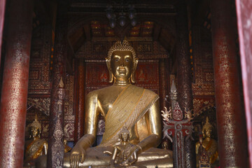 Obraz premium Serene golden Buddha statue sits in meditation inside an ancient, dark wood temple. This sacred Asian religious art piece inspires peace, faith, and spiritual tranquility