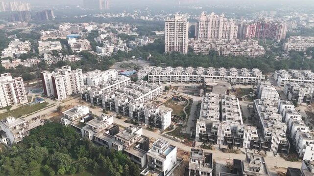 Aerial footage of a planned residential township in Greater Noida with uniform apartment blocks, central green spaces, and high-rise buildings under light NCR haze, highlighting modern urban area.