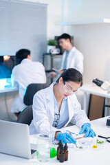 Obraz premium Woman scientist researcher examining test sample aside laptop while working with colleagues in lab.