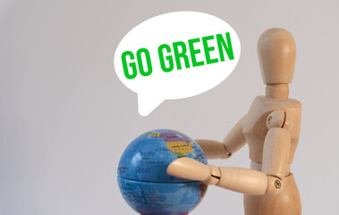 Wooden mannequin holding a globe with a speech bubble containing the words "Go Green"