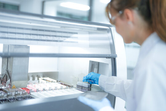 Focused female scientist loading a rack of microscope slides into an automated staining machine in a sterile laboratory. Professional researcher preparing tissue samples for pathology diagnosis.