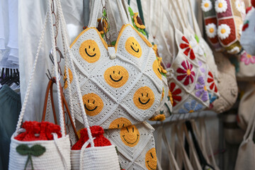 Cheerful collection of handmade crochet bag with happy smiley face pattern on display. This colorful craft accessory for sale at market has unique and creative design