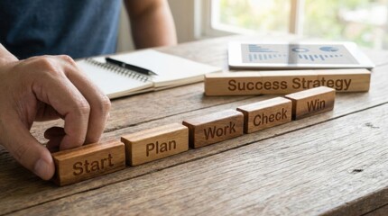 Strategy building concept showing a person's hand manipulating Start, Plan, Work, Check, and Win wooden blocks on a warm wood surface.
