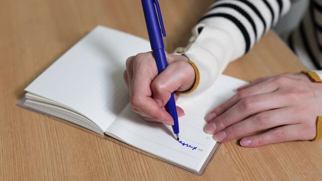 手帳に予定を書きこむ女性の手元のクローズアップ