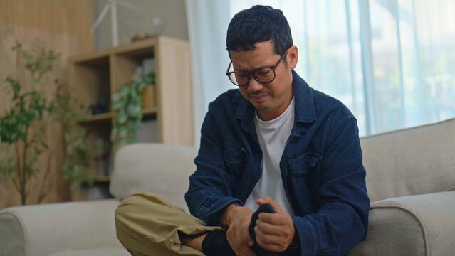 Asian Man Massaging His Painful Foot While Sitting on Sofa at Home