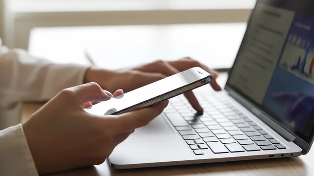 Person using a smartphone and laptop on a wooden desk 4k video