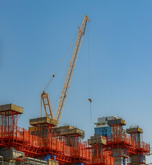 Construction site with tall crane and partially built structures under clear blue sky, showcasing urban development and industrial progress