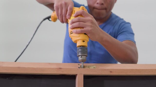 Carpenter using power drill screwing hinge into wood frame