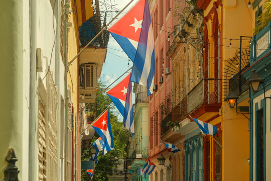 Havana, Cuba - Cuban flags hang along the sides of colorful colonial architecture in a narrow street in old town, creating a vibrant display of national pride and heritage.