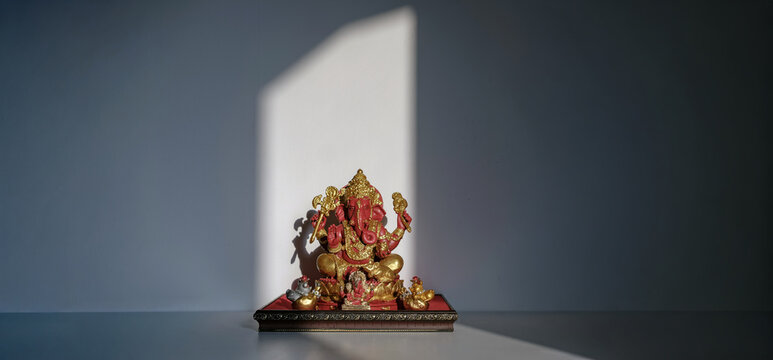 red Ganesha statue on white table with white wall background in sun light spot from window
