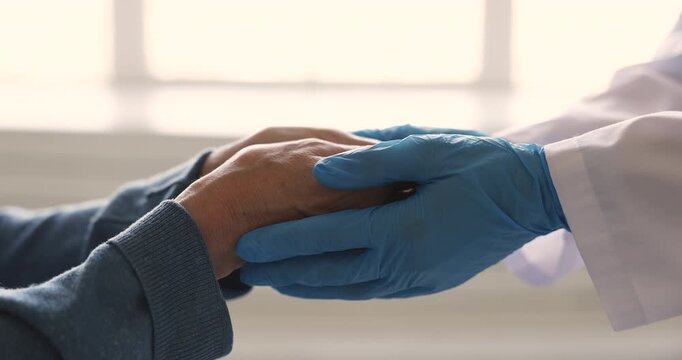 Closeup female doctor hands in rubber gloves holds, strokes of patient arms, gesture of emotional support, empathy, encouragement after disease or diagnose news. Therapy, medical health care service