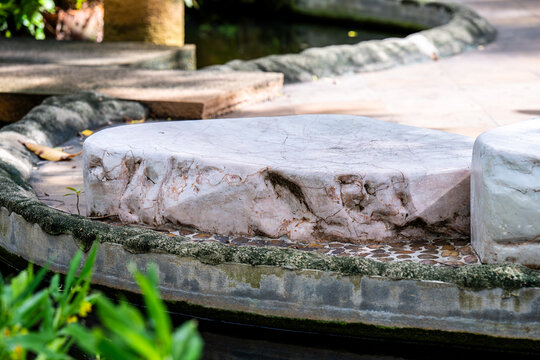 Large flat pinkish-white decorative garden stone used as a border for an outdoor walkway by a pond. Featuring natural rock textures and soft daylight in a tranquil park setting.
