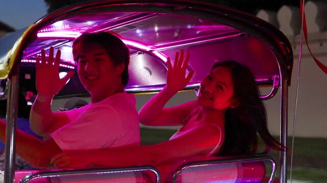 Young couple waving during colorful tuk tuk night ride