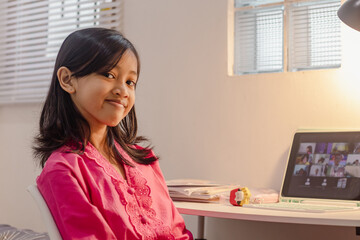 A happy Indonesian female student studying online from home using tablet computer