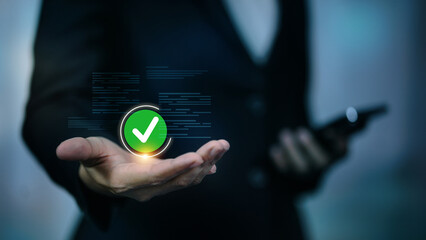 Businessman hand holding glowing green check mark icon for approved and verified concept. © vittaya