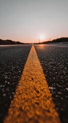 Asphalt Road with Yellow Center Line Under Golden Sunset Sky Leading to the Horizon Perspective View Dark Pavement and Tranquil Natural Landscape