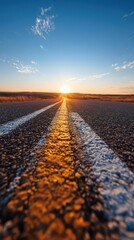 Low Angle View of Asphalt Road with White Lines Leading to Golden Sunset Under Blue Sky with Scattered Clouds in Distant Horizon Landscape
