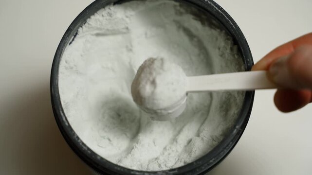 Hand scooping a full scoop of creatine from a jar, close-up, top view