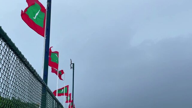 The Maldivian flag on Ukulhas Island fluttering in the wind, many Maldivian flags against a blue cloudy sky, the religion is Islam
