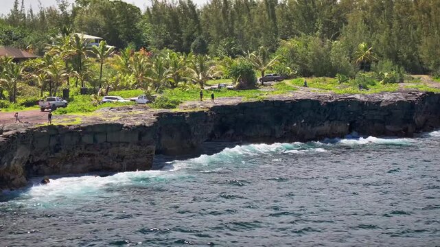 A strafing drone view of the popular Paradise Cliffs on the big island of Hawaii formed from ancient lava flows from the Kilauea volcano as waves crash and birds fly with homes and vacation rentals