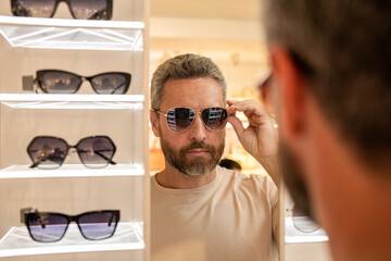 Man choosing sunglasses in shop. Sunglasses model in fashion store. Fashionable man. Trendy sunglasses accessories for men. Eyewear collection. Fashion look with sunglasses. Sunglasses fitting