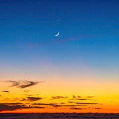Two crescent moons above a colorful sunset over clouds