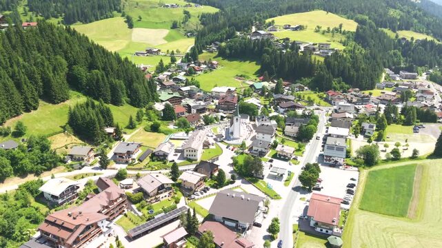 Fly over the Filzmoos Dachstein valley during summer across a village and juice green grass fields