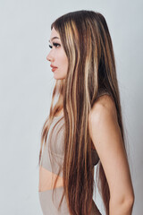 Naklejka premium Young woman with long straight hair and natural makeup in neutral outfit posing in profile on plain background. Beauty, fashion, and casual style concept with serene expression.