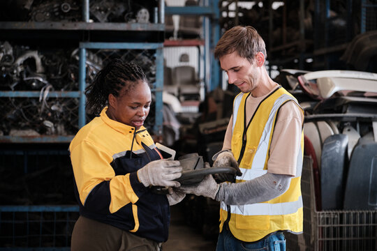 White male worker checks auto spare parts stock storage with Black female inspector at stack warehouse, working labor job in manufacturing factory, and industrial occupation for distribution business.