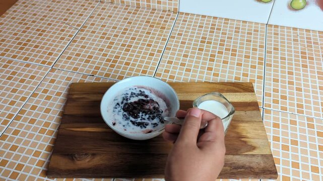Woman's hand stirring a bowl of Bubur Ketan Hitam (black sticky rice), a sweet Indonesian porridge made from black sticky rice, coconut milk, and palm or cane sugar. 4K Video. 