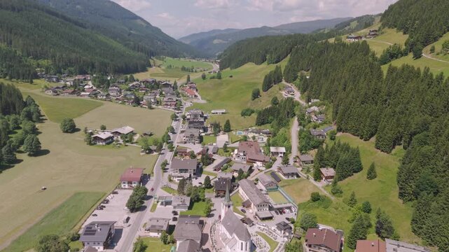 Fly over the Filzmoos Dachstein valley during summer across a village and juice green grass fields