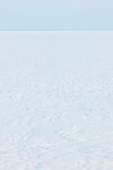 Obraz premium Expansive pristine white snow field with gentle ripples meeting a soft clear blue sky horizon
