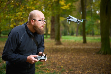 A person with a beard controls a flying drone in a vibrant park filled with colorful autumn leaves. The setting is peaceful and full of nature. © anatoliy_gleb