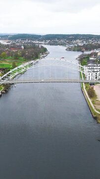 centers steel arch bridge glomma river depots rail lines apartments green spaces extend across fredrikstad norway balanced aerial composition urban infrastructure 
