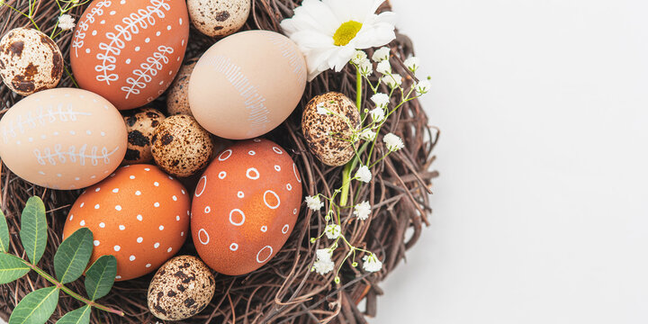 Easter nest with hand-painted eggs and quail eggs on a light background. A rustic spring composition with natural elements, fresh greenery and floral details.
