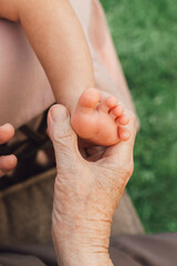 Fototapeta premium Grandmother and mother holding newborn baby feet in their hands outdoors. Three generations.