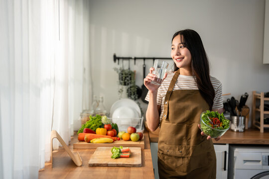 Asian woman eatting healthy salad and drink water in kitchen at home.