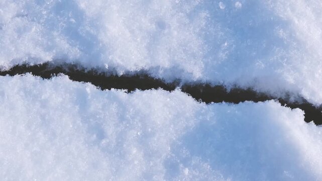 Horizontal dark fissure breaking through a pristine white snow surface on a cold winter day