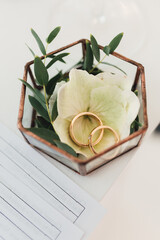 Gold wedding rings in a glass geometric box with eucalyptus and flowers