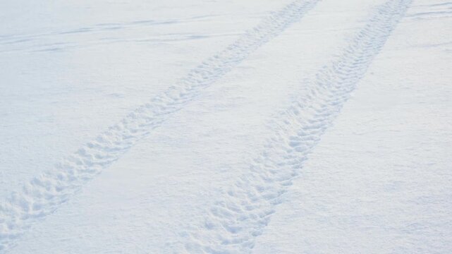 Clear fresh parallel vehicle tire tracks pressed into vast pristine white snow surface in winter