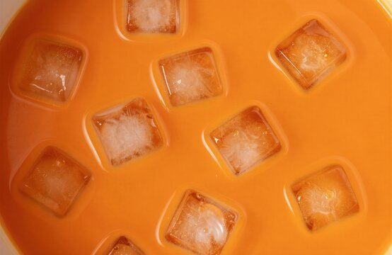 Primer plano de cubitos de hielo flotando en un l&iacute;quido anaranjado brillante.