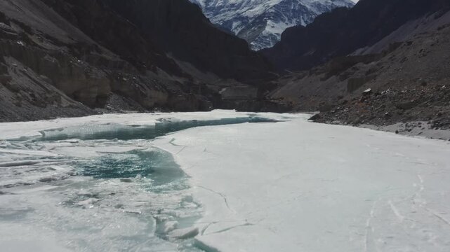 Partially frozen Zanskar River shows turquoise water cracks amid thick ice sheets flanked by dramatic snow-capped canyon walls in Ladakh, India.
