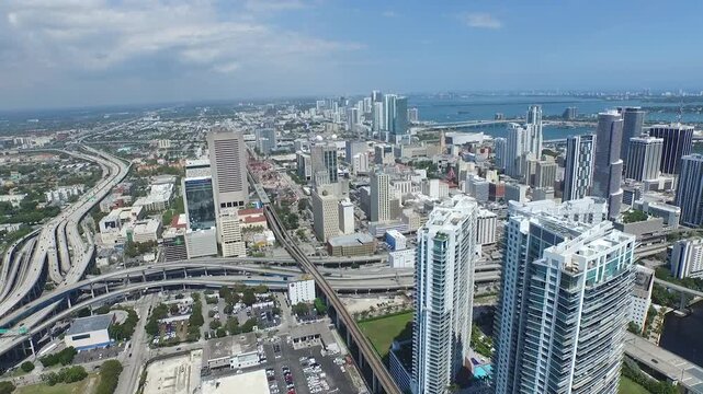 Drone pulls back over Miami showing skyscrapers, busy highways and the bay on a sunny day.