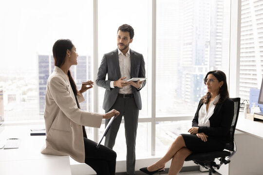 Young New Zealander team leader clarifying project details during group briefing with diverse workmates, working together on strategy, exchanging ideas and solution gathered in modern coworking office