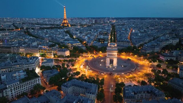 Aerial night view of the famous landmark Triumphal Arch or Arc de Triomphe and Eiffel Tower surrounded by busy streets and lush greenery in the heart of the city Paris, France. Drone orbiting flight