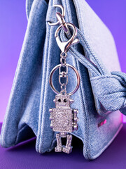 Close-up of a bright metal keychain in the shape of a white robot made with rhinestones on a blue bag