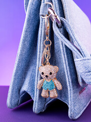 Close-up of a bright metal keychain in the shape of a blue teddy bear made with rhinestones on a blue bag