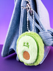 Close-up of a soft plush keychain in the shape of a green avocado on a blue bag.