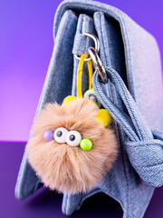 Close-up of a soft, fluffy plush keychain in the shape of a brown monster with eyes on a blue bag.