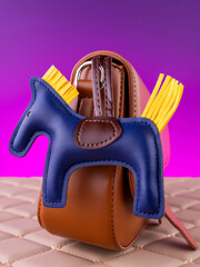 Close-up of a bright leather keychain in the shape of a blue horse with a saddle on a brown  bag